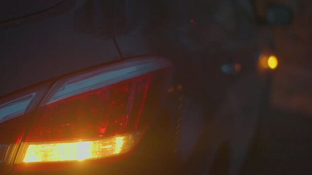Close-up of a car's tail light and turn signal illuminated in the dark, creating a blurred and moody atmosphere, the red and amber lights contrast against the dark background