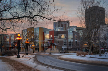 Winter evening view of Waterfront Drive at the corner of Bannatyne Avenue with warm streetlights along the sidewalk in the foreground and the skyscrapers of Downtown Winnipeg in the background
