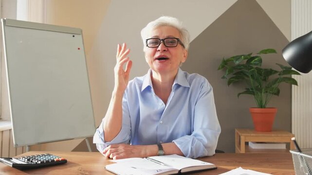 Middle aged senior woman boss leader discussing with team in online meeting. Older mature businesswoman in office speak talk on video call discussing project ideas. Headshot selfie webcamera view