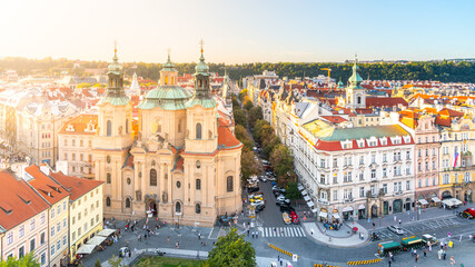 Obraz premium The golden sunlight bathes the Church of Saint Nicholas and surrounds Old Town Square, highlighting the Baroque architecture and casting warm tones over the bustling city square. Prague, Czechia