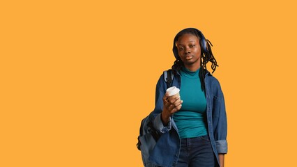 Young girl with backpack and headphones yawning, feeling tired, drinking coffee to wake up. Sleepy...