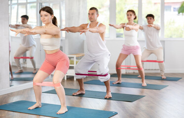Obraz premium Group of women and men standing and doing stretching exercise with resistance bands in modern fitness studio