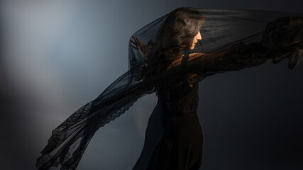 A Gothic bride, a mysterious Halloween image, a Gothic gloomy aesthetic. An elegant young woman in a black dress and with a veil on her face