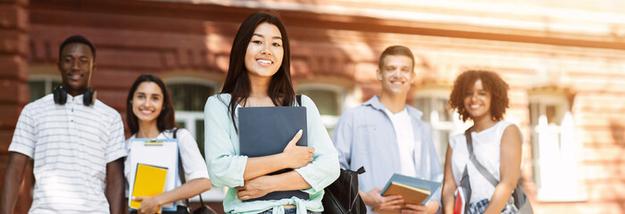 University life. Happy asian student girl holding books and smiling, posing outdoors with her...