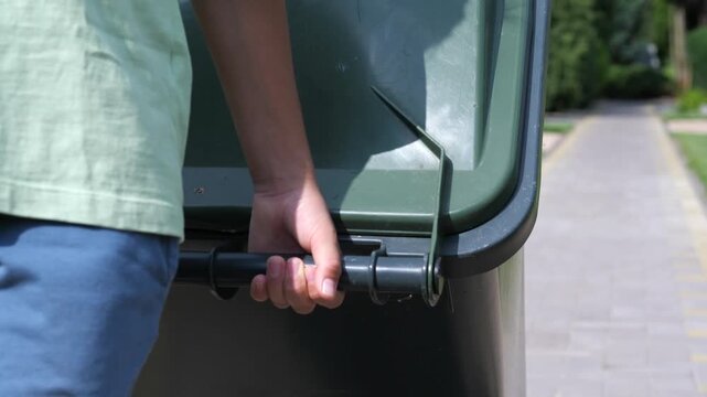 lose-up of a boy putting a trash can for garbage collectors