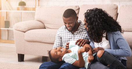 Family fun. Loving african american parents tickling their little daughter, enjoying spending time...
