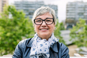 Smiling portrait of senior woman looking at camera outdoor. Head shot of 60 year old woman over...