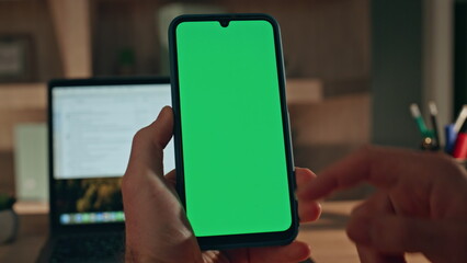 Man finger tapping chroma key cellphone at home workplace with laptop close up.