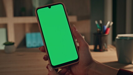 Woman hands holding greenscreen mobile phone at home evening close up. 