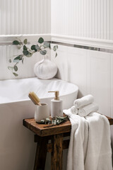 Fresh towels, soap dispenser bottle and holder with massage brush on wooden bench bathroom
