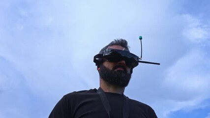 FPV drone man pilot in a copter headset outdoor blue sky. Caucasian male copter vr operator learnig to fly in aircraft school training ground polygon area - Powered by Adobe