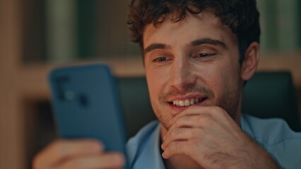 Carefree freelancer browsing video content at cellphone in evening home close up