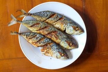 Fried mackerel in a white plate on a wooden table, healthy seafood concept, copy space.