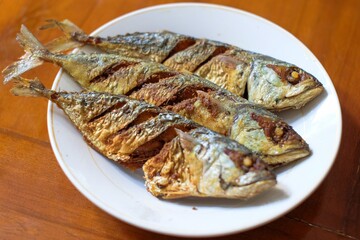Fried mackerel in a white plate on a wooden table, healthy seafood concept, copy space.