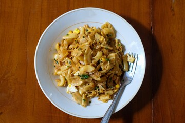 Stir fried spicy macaroni on white platree with fork, in the wood table, homemade food.