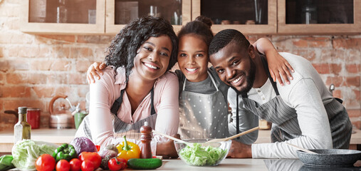 Happy african family embracing at kitchen while making healthy dinner, copy space