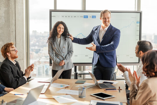 A group of business professionals gathered around a conference table in a modern office space are applauding a young lady colleague who has just finished giving a presentation - Powered by Adobe