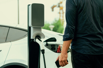 Man using smartphone online banking application to pay for electric car battery charging from EV...
