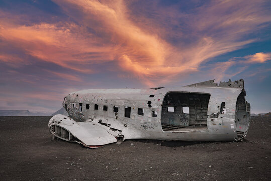 The weathered fuselage of a US Navy Douglas DC-3 plane on Solheimasandur beach in Iceland, with dramatic clouds and colorful sky creating a striking contrast.