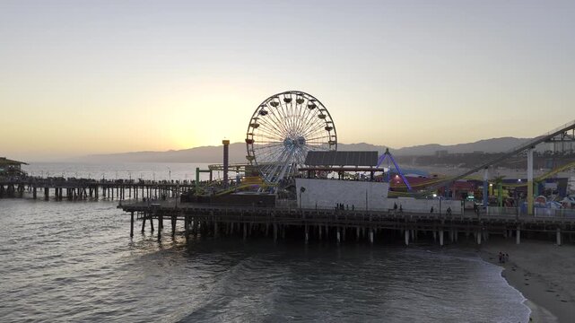 Ferris Wheel on Santa Monica Pier at sunset. HDR drone footage rising up for aerial view over iconic pier theme park.