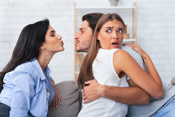 Love Triangle And Jealousy. Cheating Boyfriend Kissing A Girl While Hugging His Girlfriend Sitting...