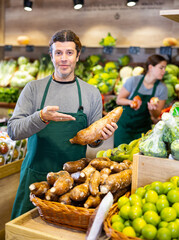 Adult man in apron sells cassava in vegetable shop