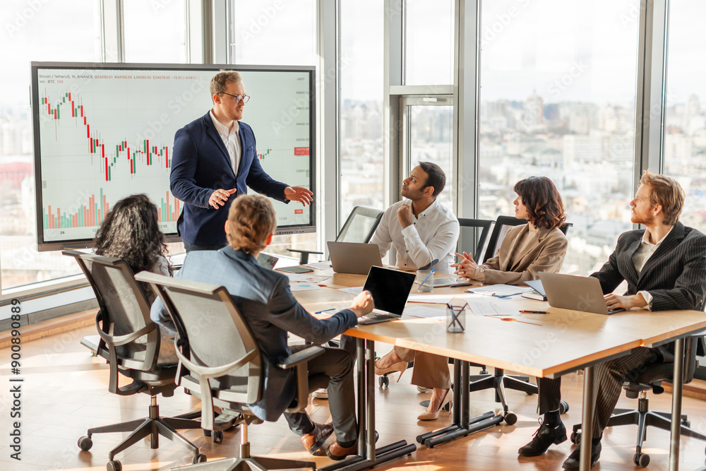 Poster A businessman is presenting financial data to a team in a modern office with large windows overlooking the city. He is standing and pointing at a chart on a screen