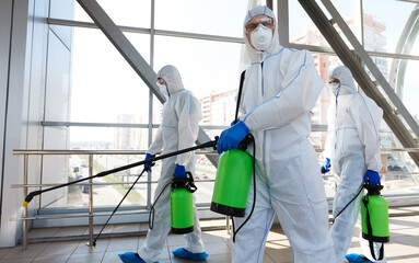 Professional workers in hazmat suits disinfecting indoor accommodation, pandemic health risk, coronavirus