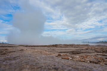 A striking geothermal landscape in Iceland featuring a large steam plume rising from the ground,...