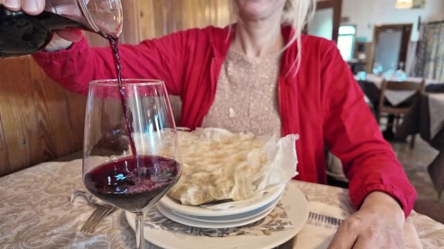 SLOW MOTION: pouring glass of wine in a crystal clear glass, as she savors a Borlengo. traditional dish, a symphony of meat and cheese, hails from the Emilia-Romagna region in Italy