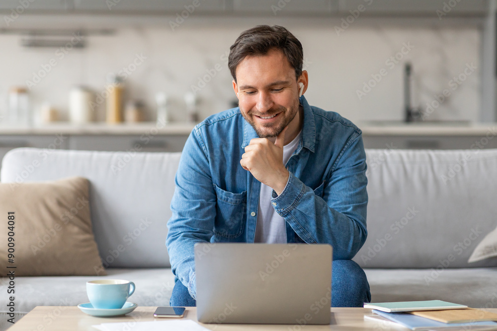 Aufkleber a man in a blue shirt sits on a white couch and looks at a laptop in his lap. he has one hand on his