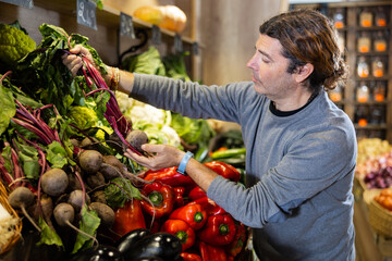 Satisfied man chooses beets in the vegetable section of the supermarket