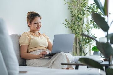 Smiling young woman freelancer sitting on couch and using laptop, remote work or studying online.