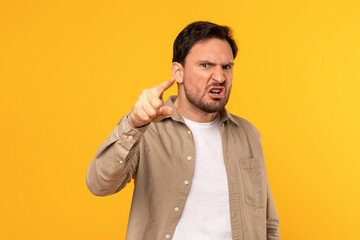 A man is shown in a studio, wearing a light brown button-down shirt over a white t-shirt, looking...