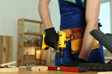 Craftsman working with drill at wooden table in workshop, closeup. Space for text