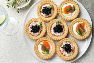Delicious canapes with salmon, caviar, microgreens and glass of water on beige textured table, flat lay