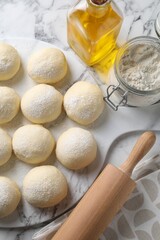 Raw dough balls, flour, rolling pin and oil on white marble table, top view