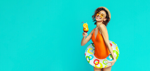 African American happy woman in an orange swimsuit is holding a cocktail and a colorful inflatable ring. She is wearing a straw hat and sunglasses, and has a bright smile on her face.