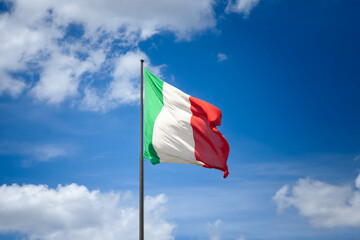 Selective bur on Italian flag waving in the air against a blue sky in Italy, representing national...