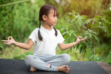 A little girl practices yoga in the backyard, surrounded by the refreshing embrace of nature.