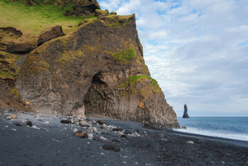 A stunning coastal scene at Reynisfjara black sand beach in Iceland, featuring rugged cliffs with basalt columns and the dramatic Reynisdrangar sea stacks.