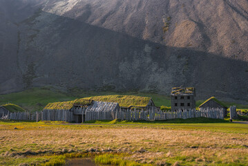 Rustic, abandoned Icelandic building with grass-covered roofs and wooden fence, set against a large barren mountain, showcasing Iceland's cultural heritage.