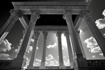 Fototapeta premium A black-and-white photograph of an intricately carved classical structure with tall columns, captured from a low angle. The sky in the background features scattered clouds.