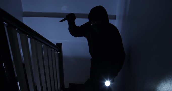 A thief in a black cloak and gloves sneaks into a house at midnight, holding a knife and flashlight, with the intent to harm the occupants.
