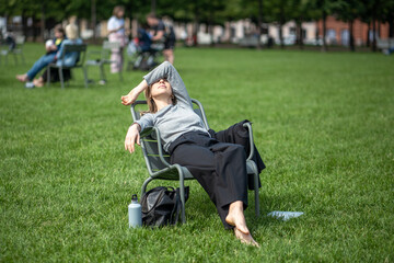 Tired woman takes break relaxed sitting barefoot in public space on lawn. Work-weary businesswoman...