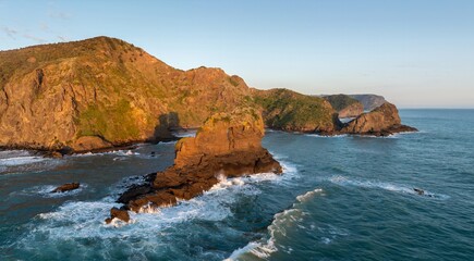 Rocky coastline, ocean waves and rocky island at Anawhata at sunset, Piha, Auckland, New Zealand.