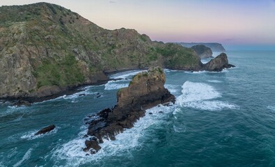 Rocky coastline, ocean waves and rocky island at Anawhata at sunset, Piha, Auckland, New Zealand.
