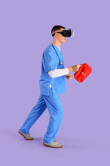 Male doctor with first aid kit using VR glasses on lilac background