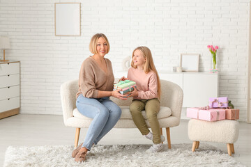 Beautiful young woman and her cute little daughter with books sitting on sofa in living room