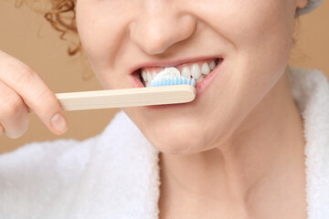 Beautiful young woman brushing teeth on brown background